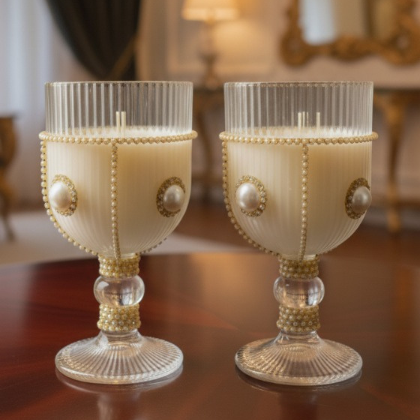 Two decorative candles in glass holders with pearl-like embellishments on a wooden surface.