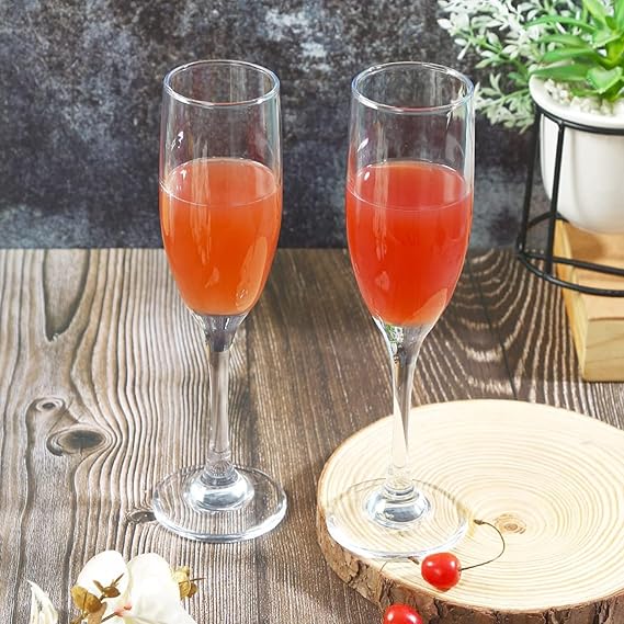 Two champagne flutes with red cocktails on a wooden surface with decorative elements.