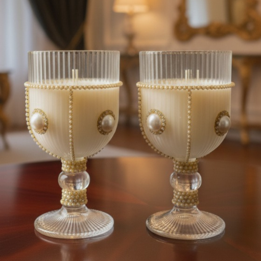 Two decorative candles in glass holders with pearl-like embellishments on a wooden surface.