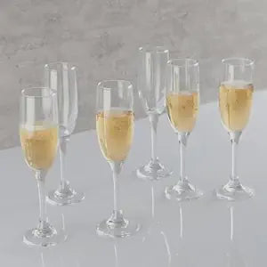 Set of six champagne flutes with champagne on a gray surface