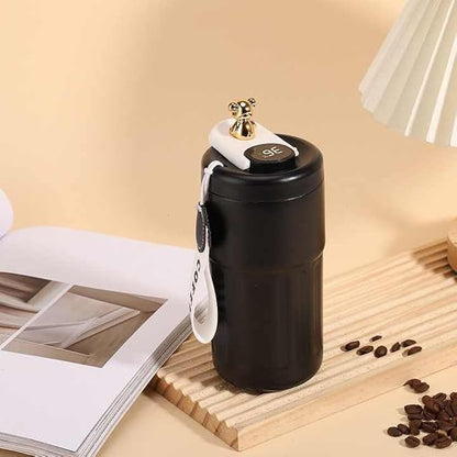 Black portable coffee grinder on a wooden surface with coffee beans and an open book in the background.
