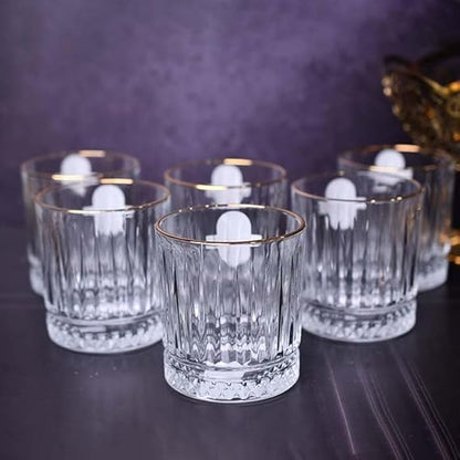 Set of clear glass tumblers with gold rims on a dark surface.