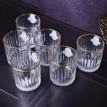Set of six clear glass tumblers with gold rims on a dark surface.