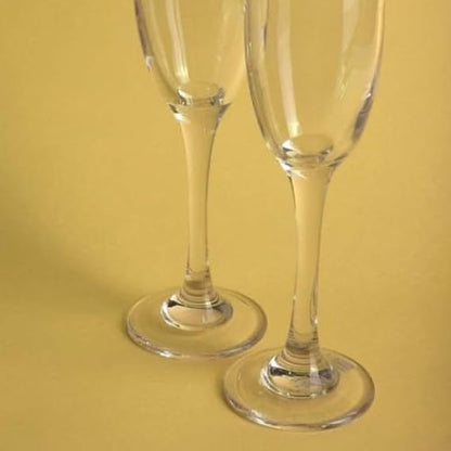 Two clear champagne flutes on a yellow background
