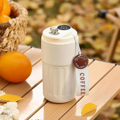 White coffee tumbler with a brown tag on a wooden surface with oranges and leaves.