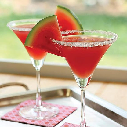 Two red cocktails with watermelon slices in martini glasses on a blurred outdoor background.