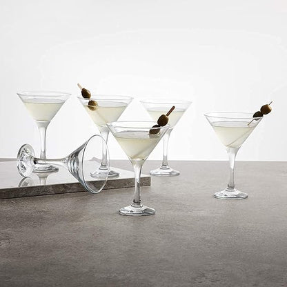 Five martini glasses with olive garnishes on a gray surface.