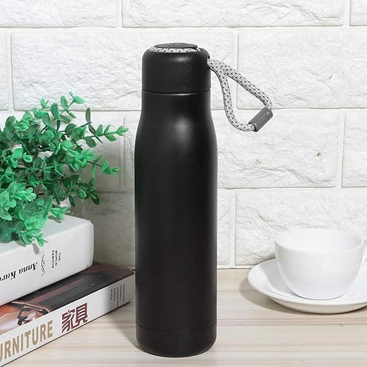 Black insulated bottle with a handle on a wooden surface with a white brick wall background