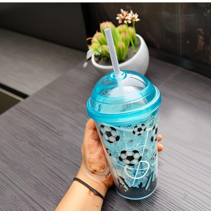 Hand holding a blue tumbler with soccer ball pattern on a table with a plant in the background