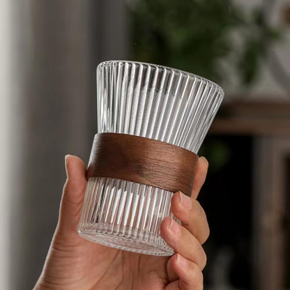 Clear glass candle holder with a brown band held by a hand against a blurred indoor background