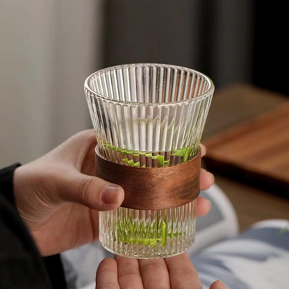 Clear glass cup with wooden band held by a hand, blurred background