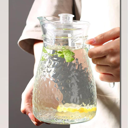 Clear glass pitcher filled with lemon slices and mint leaves, held by a person.