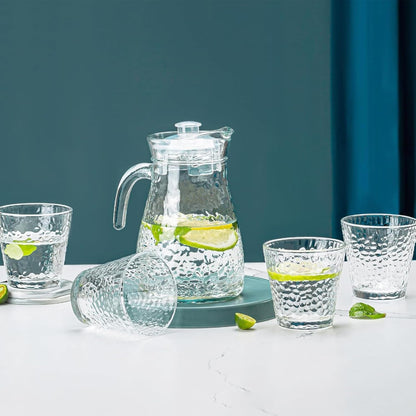 Clear glass pitcher and cups with lime slices on a white surface against a blue background