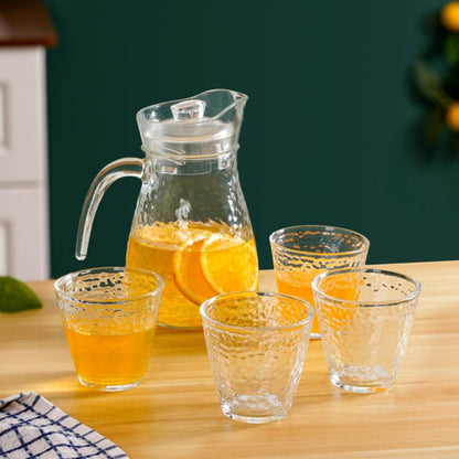 Clear glass pitcher and four glasses filled with orange juice on a wooden table.