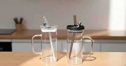 Two clear glass mugs with lids and straws on a wooden surface.