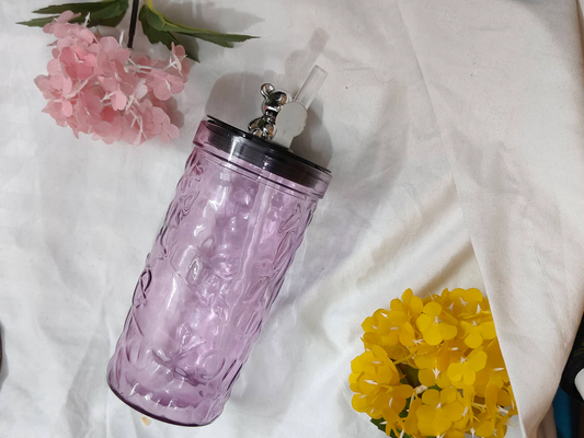 Pink textured tumbler with a straw on a white fabric background with flowers.